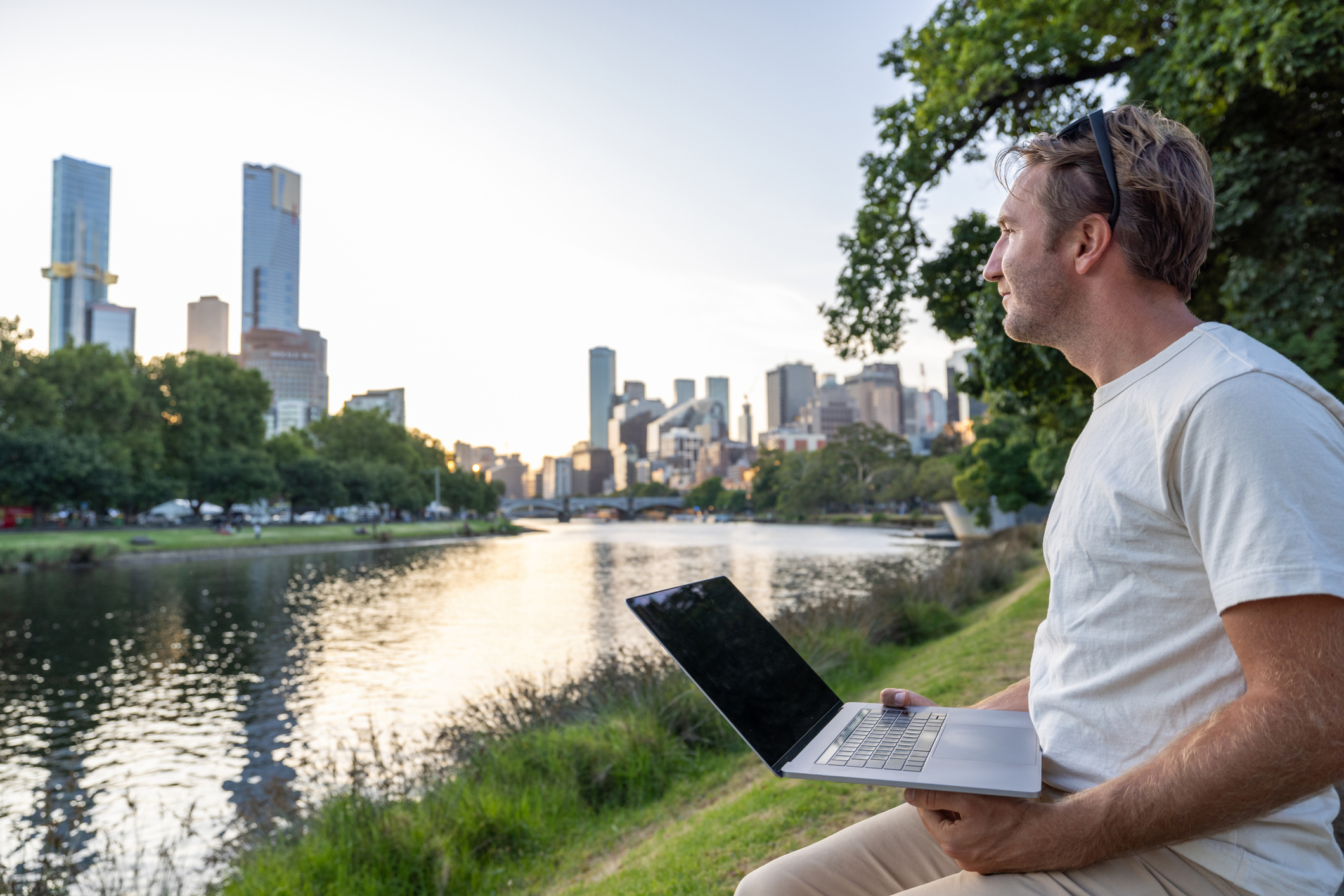 A young man is working on a laptop near a park in Melbourne. 